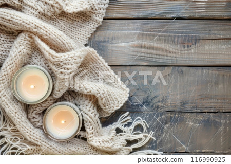 Cozy knit blanket wrapped around two lit candles on rustic wooden table, copy space. Generative AI 116990925
