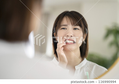 A woman in her 30s checking her gums while brushing her teeth 116990994