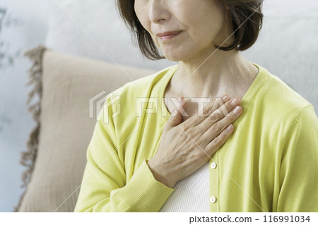 A middle-aged woman holding her breasts while sitting in the living room A middle-aged woman holding her breasts while sitting in the living room 116991034