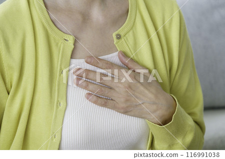 一位中年婦女坐在客廳裡，抱著乳房 116991038
