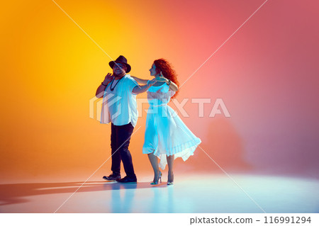 Joy and energy of Latin dance. Practicing salsa with enthusiasm, pair refines their dance-skills in neon light against gradient background. Joy and energy of Latin dance. Practicing salsa with enthusiasm, pair refines their dance-skills in neon light against gradient background. 116991294