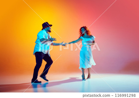 Salsa dancers practice with passion in neon light against gradient orange background, showing their feelings throw moves. 116991298