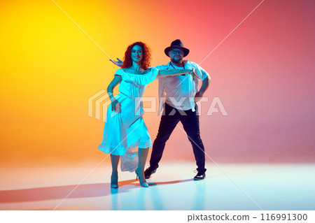 Salsa practice. Dancers, man and woman, refine their technique and fluidity in neon light against gradient orange background. Salsa practice. Dancers, man and woman, refine their technique and fluidity in neon light against gradient orange background. 116991300