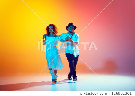Salsa duo rehearses with energy, focusing on perfecting their rhythm and synchronization in neon light against gradient orange background. Salsa duo rehearses with energy, focusing on perfecting their rhythm and synchronization in neon light against gradient orange background. 116991301