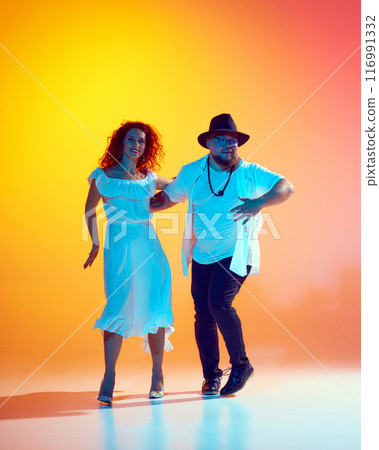 Couple dancers rehearses with energy, focusing on fluid movements and rhythmic precision in neon light against gradient orange background. 116991332