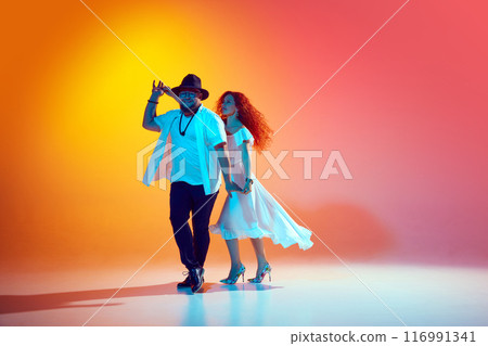 Joyful Latin dancers rehearse with intensity, perfecting their salsa steps and rhythms in neon light against gradient orange background. 116991341