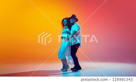 Latin dancers enjoy dance, perfecting their salsa steps and rhythms in neon light against gradient orange background. 116991343