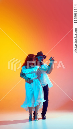 Practicing salsa with enthusiasm, this pair sharpens their skills in neon light against gradient orange background. Dynamic nature of Latin dance. 116991344