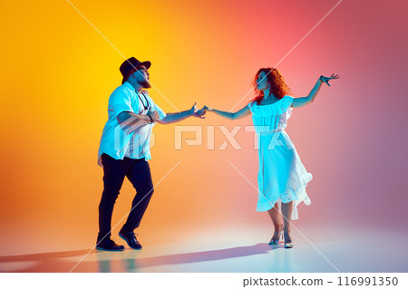 Practicing lively steps of salsa, duo perfects their rhythm and coordination in neon light against gradient orange background. Practicing lively steps of salsa, duo perfects their rhythm and coordination in neon light against gradient orange background. 116991350