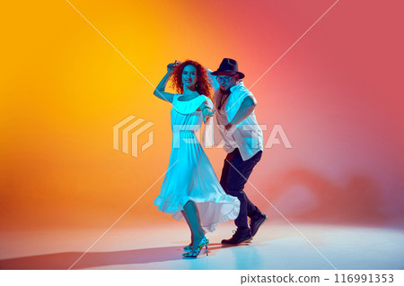 Salsa dancers, couple rehearse with vigor, refining their technique, their steps in neon light against gradient orange background. 116991353