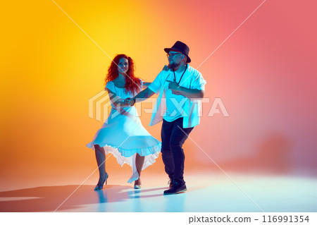 Focused on salsa training, dance couple work on precision and fluidity during practice session in neon light against gradient orange background. Focused on salsa training, dance couple work on precision and fluidity during practice session in neon light against gradient orange background. 116991354