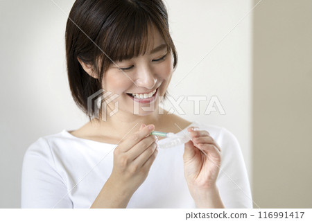 Home whitening image: A young woman holding medicine and a mouthpiece 116991417