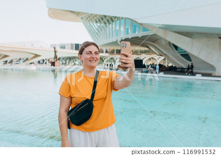 Young traveling woman taking selfie outdoors. Concept of travel, tourism and vacation in city. Ciudad de las Artes y las Ciencias de Valencia.Valencia City of Arts and Sciences. High quality photo 116991532