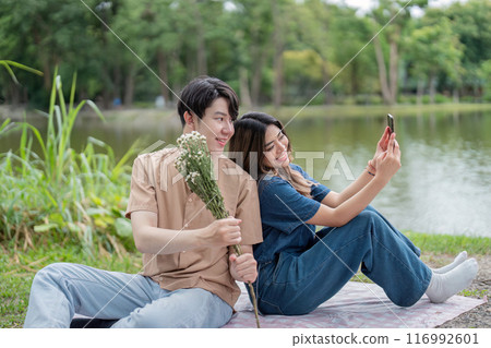 Happy Couple Enjoying a Relaxing Picnic by the Lake in a Beautiful Park Setting Happy Couple Enjoying a Relaxing Picnic by the Lake in a Beautiful Park Setting 116992601