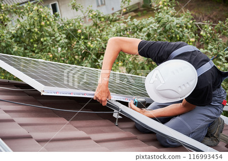 Man measuring photovoltaic solar panels with tape measure. Male worker taking measurements before installing solar modules on roof of house for generating electricity through photovoltaic effect. Man measuring photovoltaic solar panels with tape measure. Male worker taking measurements before installing solar modules on roof of house for generating electricity through photovoltaic effect. 116993454