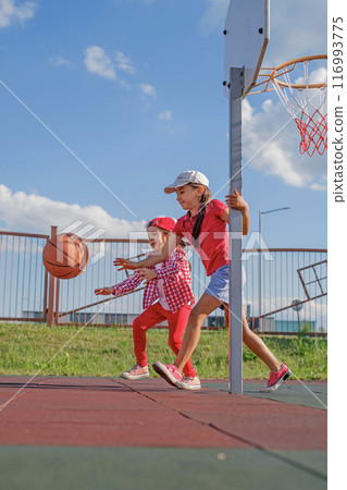 Preschool girls catch up with the ball in a basketball game. Children have fun running on the playground Preschool girls catch up with the ball in a basketball game. Children have fun running on the playground 116993775