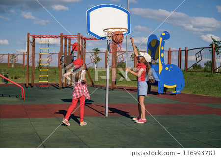 Little girls play basketball on an outdoor summer playground, clearly throwing ball into the basket 116993781