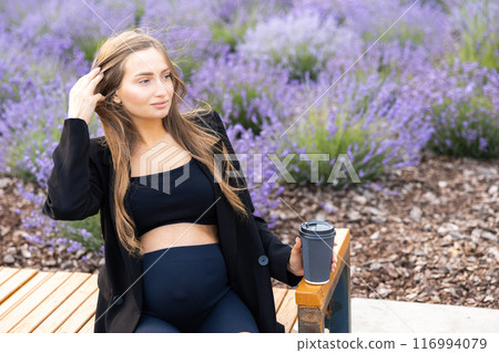 Pregnant woman sits on bench in the park holding cup of coffee Pregnant woman sits on bench in the park holding cup of coffee 116994079