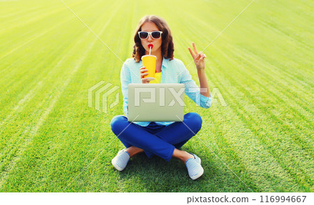 Woman drinking juice with laptop in the park on green grass background 116994667