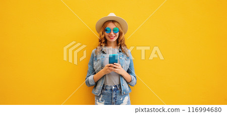 Summer portrait of happy young woman with mobile phone looking at device on yellow background 116994680