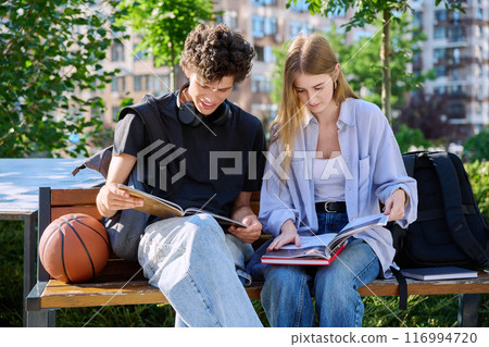 Teenage college students guy and girl talking, sitting outdoor near educational building. 116994720