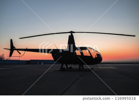 Helicopter silhouette against vibrant sunset at airport landing strip 116995018