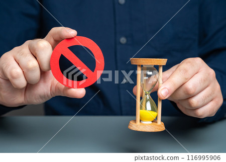 A man holds a red NO sign and an hourglass. Time is running out. Deadline approaches. Important prohibition must be adhered to without delay. Temporary restriction for a limited time. A man holds a red NO sign and an hourglass. Time is running out. Deadline approaches. Important prohibition must be adhered to without delay. Temporary restriction for a limited time. 116995906