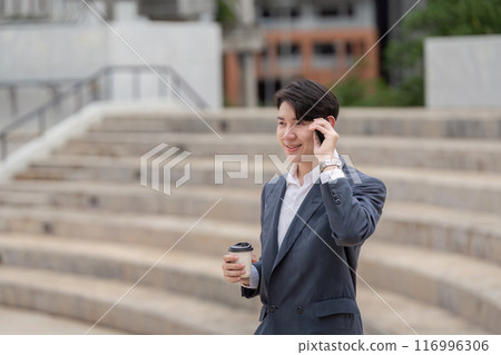 Young Professional Businessman Talking on Phone and Holding Coffee in Modern Urban Setting 116996306