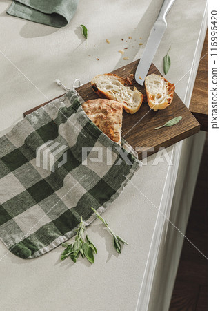 Sliced bread in linen bag on wooden board, fresh herbs and stainless still kitchen knife. Kitchen aesthetic concept Sliced bread in linen bag on wooden board, fresh herbs and stainless still kitchen knife. Kitchen aesthetic concept 116996420