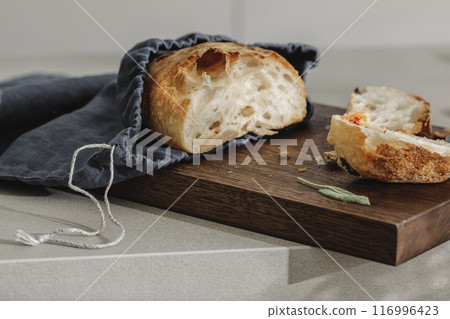 Sliced bread in linen bag on wooden board, fresh herbs and stainless still kitchen knife. Kitchen aesthetic concept Sliced bread in linen bag on wooden board, fresh herbs and stainless still kitchen knife. Kitchen aesthetic concept 116996423