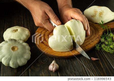 Cooking zucchini on the kitchen table by a man. Cutting vegetable marrow with a knife before frying or stewing at home Cooking zucchini on the kitchen table by a man. Cutting vegetable marrow with a knife before frying or stewing at home 116996543