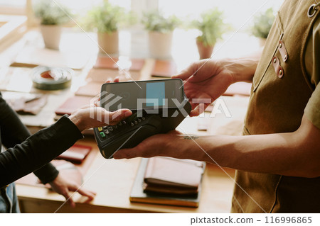 Customer tapping her phone to pay via terminal while male hands holding it 116996865