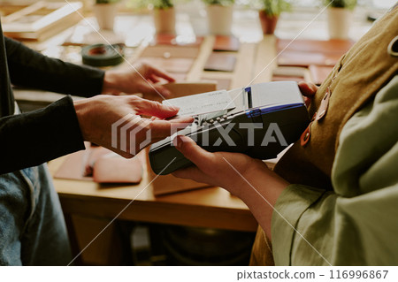 Male hands tapping credit card to buy leather goods while female hands holding payment terminal 116996867