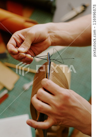 Unrecognizable male hands sewing stitches painstakingly to create leather card holder Unrecognizable male hands sewing stitches painstakingly to create leather card holder 116996878