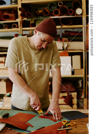 Male tailor using knife to cut leather fabric in old atelier 116996885