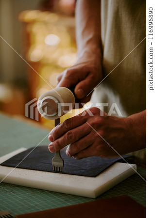 Medium close up of unrecognizable male hands poking black colored piece of leather 116996890