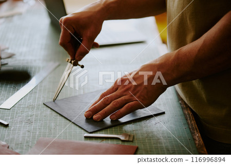 Medium close up of unrecognizable male hands holding leather piece while poking it 116996894