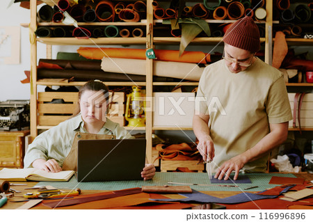 Male tailor cutting out details while his female colleague with down syndrome taking notes Male tailor cutting out details while his female colleague with down syndrome taking notes 116996896