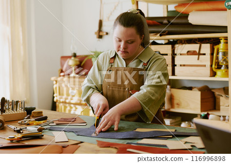 Female atelier worker with down syndrome cutting out leather details very carefully Female atelier worker with down syndrome cutting out leather details very carefully 116996898