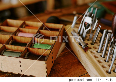 Medium close up of wooden box with multicolored spools of threads and metal nozzles for punch machine 116996910