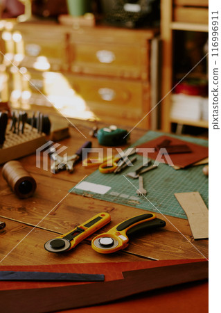 High angle shot of round knifes, leather punches and workpieces on old shabby wooden table 116996911