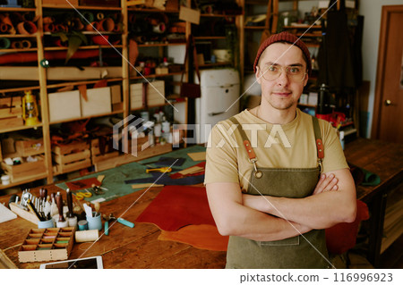 High angle portrait of male atelier worker with crossed arms surrounded by storages with huge number fabric rolls and old workspace with equipment 116996923