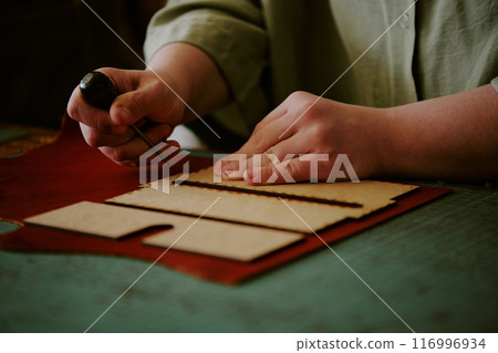 Medium close up of unrecognizable female hands poking leather piece with use of awl Medium close up of unrecognizable female hands poking leather piece with use of awl 116996934