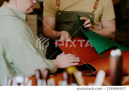 Medium close up of female client choosing natural leather while male tailor demonstrating leather 116996957