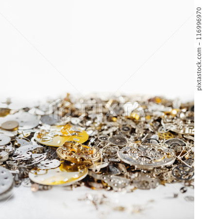 Gears, clock faces and metal parts of internal mechanism of the watch lie in heap on white background. Gears, clock faces and metal parts of internal mechanism of the watch lie in heap on white background. 116996970