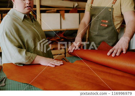 Unrecognizable man and woman with down syndrome touching natural leather while choosing material to sew leather bag 116996979