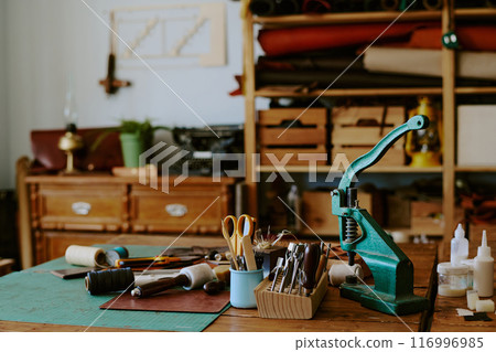Turquoise leather punch machine with sewing tools on old wooden table in atelier 116996985