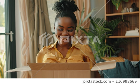 A happy young woman opening a box with a delighted expression A happy young woman opening a box with a delighted expression 116998669
