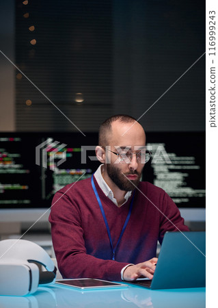Vertical portrait of man wearing glasses and using computer at desk in IT development office 116999243