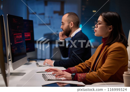 Side view portrait of young woman as female computer programmer working late in cybersecurity department lit by blue light Side view portrait of young woman as female computer programmer working late in cybersecurity department lit by blue light 116999324